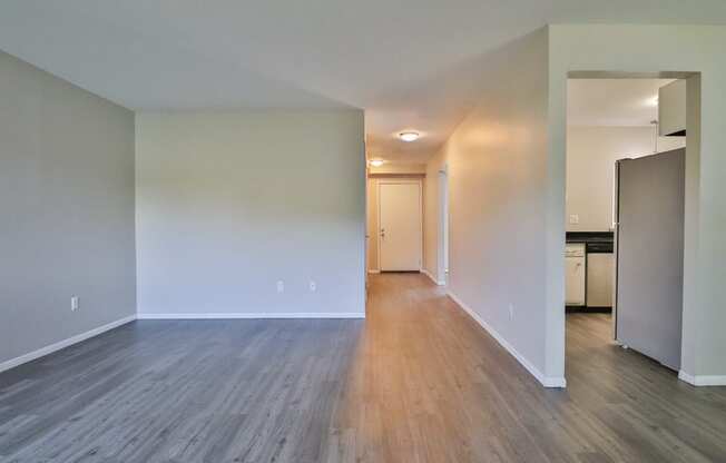 an empty living room with wood flooring and a kitchen