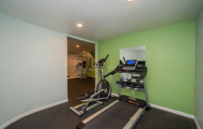 A treadmill and a stationary bike are in a room with green walls.