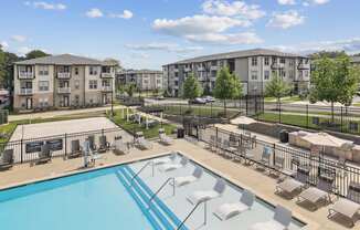 A swimming pool surrounded by sun loungers and apartment buildings.
