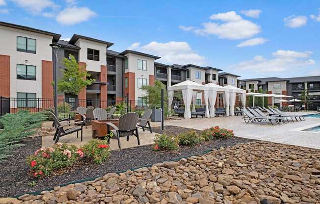 Modern 49 West Apartment complex with a poolside area includes lounge chairs, white cabanas, and a fire pit surrounded by chairs, evoking relaxation under a blue sky.