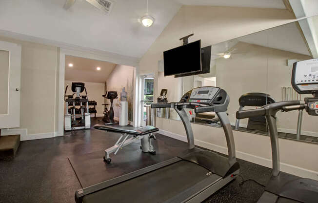 A well-equipped fitness center here at Adagio featuring treadmills, an adjustable workout bench, and strength training machines set on durable flooring, complemented by mirrored walls, mounted televisions, and overhead lighting, creating a bright, functional space designed for cardio workouts, strength training, and everyday fitness routines.