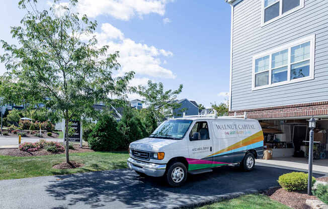 A white van with a rainbow stripe is parked in front of a house.