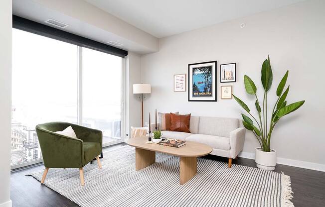 a living room with floor-to-ceiling windows and a Midcentury-inspired couch and a chair at The Bohen Luxury Apartments for Rent Minneapolis