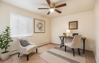 A room with a ceiling fan, a chair, a desk, and a potted plant.