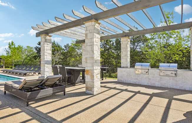 A poolside area with a pergola and lounge chairs.