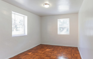 A room with wooden flooring and two windows.