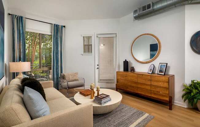 A living room with a beige couch, a round mirror, and a wooden cabinet.