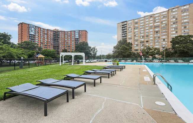 A swimming pool with a sunbed area in front of apartment buildings.