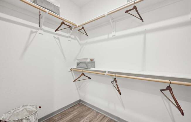 a white closet with hangers on the wall and a basket on the floor