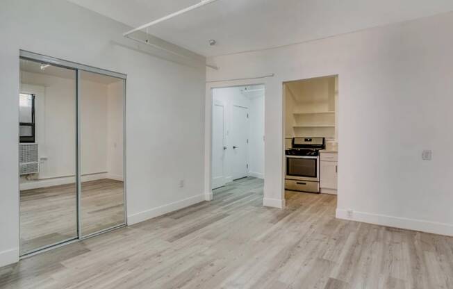 A room with a wooden floor and a kitchenette in the corner.
