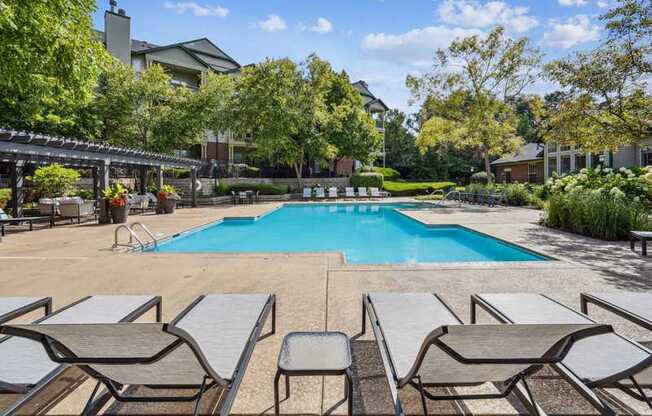 A pool surrounded by lounge chairs and trees.