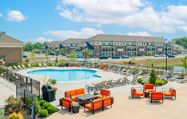 an outdoor pool with orange chairs and tables and a building in the background