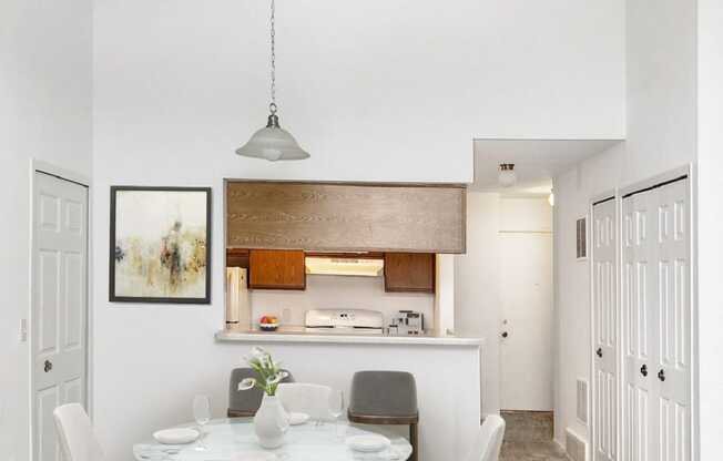 a dining area with a white table and chairs and a kitchen in the background