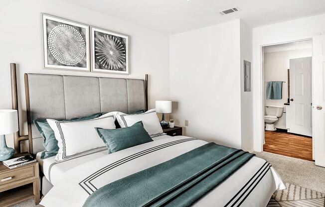 Virtually staged bedroom with carpet, accent rug, with bathroom in background featuring wood flooring