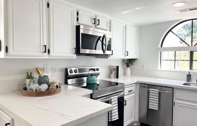 a white kitchen with stainless steel appliances and white cabinets  at The Resort at Encinitas Luxury Apartment Homes, California