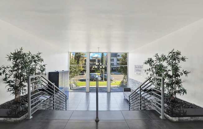 A white hallway with a plant on each side and a glass door in the middle.