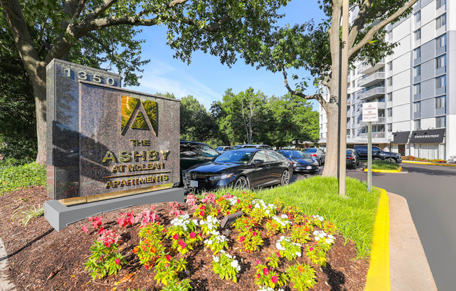 A sign for Ashby Apartments is surrounded by flowers and sits in front of a parking lot.