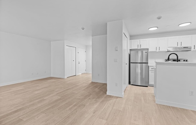 the living room and kitchen of an apartment with white walls and wood flooring