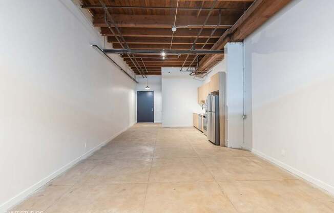 A long, empty hallway with a door at the end and a refrigerator on the side.