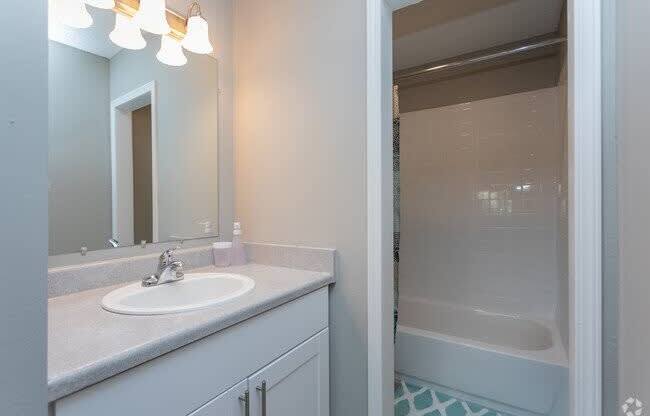 A bathroom with a sink, mirror, and shower.