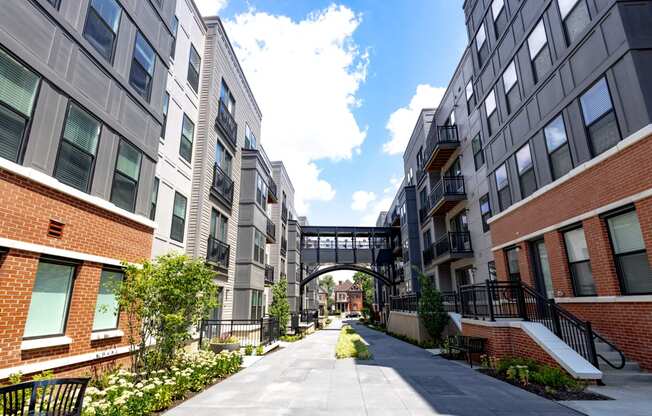 a walkway between two apartment buildings with a bridge in the background