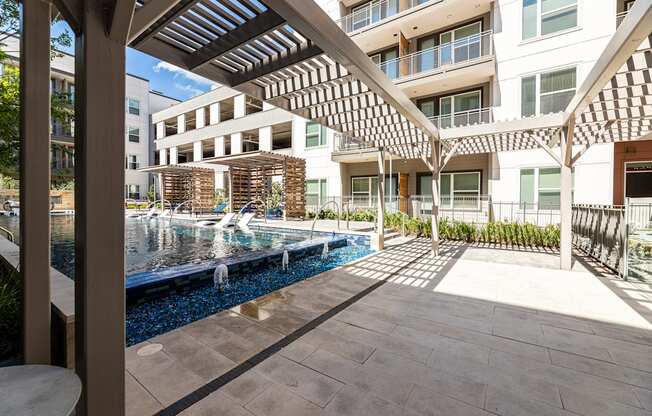 A modern building with a pool and a wooden pergola.