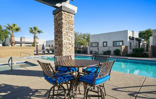 A table with chairs is in the foreground of a pool area.