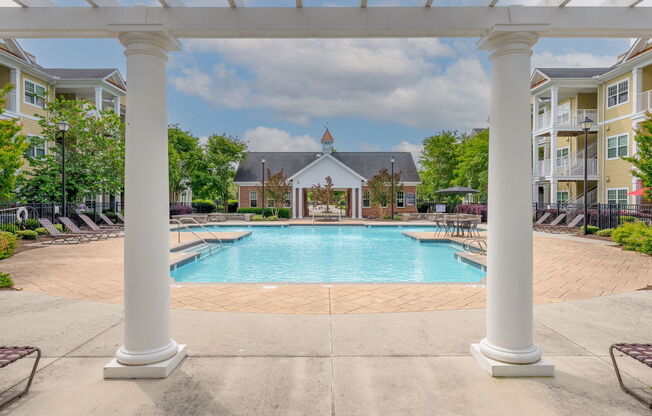 beautiful pool deck with pergola, lounges, surrounded by lush trees and apartments