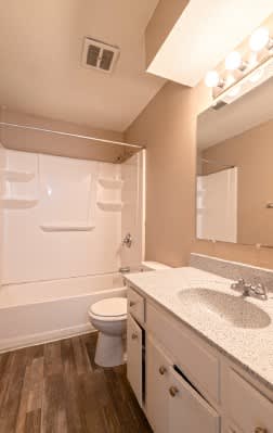 A white toilet sits in a bathroom with wood floors and a white sink.