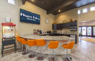 the clubhouse has a large counter with orange bar chairs and a refrigerator