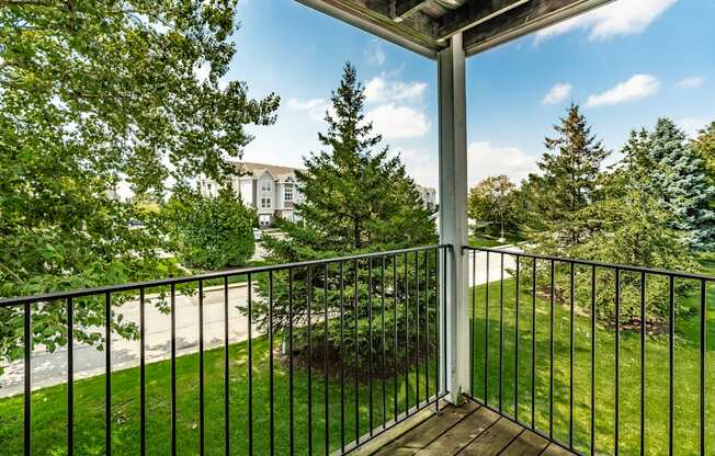 A balcony with a black railing and a view of a tree and a building in the background