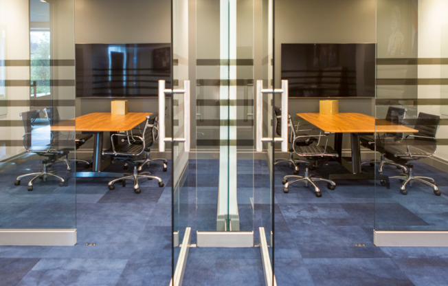 Two glass-walled conference rooms, each with a large HDTV on the wall and four rolling leather chairs around a conference table.