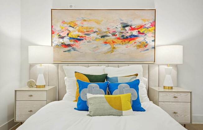 a bedroom with a bed with colorful pillows and a painting above it at Link Apartments® Calyx, Chapel Hill, NC