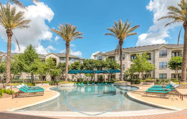 A swimming pool surrounded by palm trees and lounge chairs.