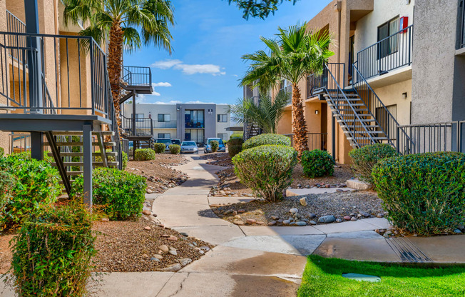 a pathway between two apartment buildings with palm trees