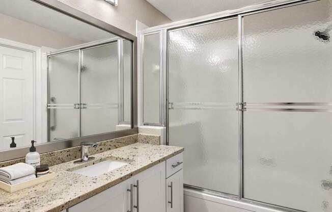 A bathroom with a sink, mirror, and shower.