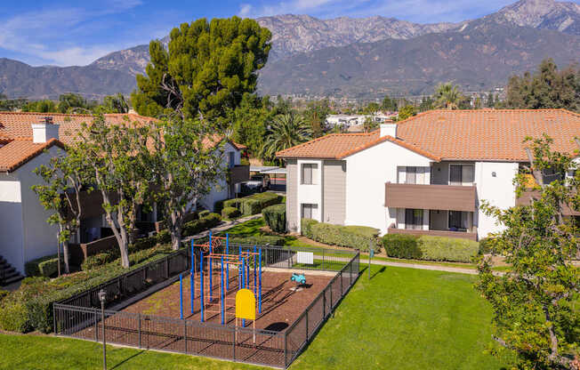 A playground with a swing set in a grassy area in front of a house.