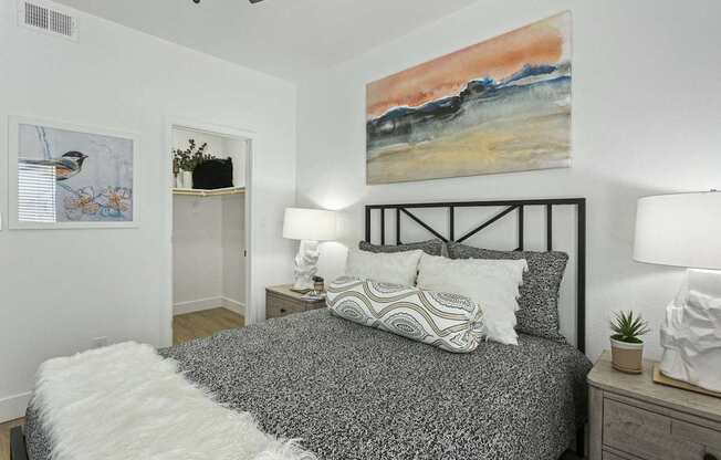 A bedroom with a bed, two lamps, and a painting on the wall.