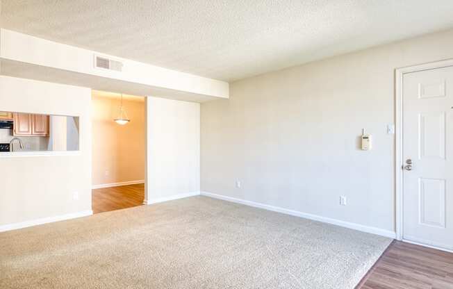 an empty living room with a white door and a kitchen