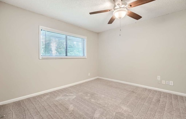 A room with a ceiling fan and a window with blinds.