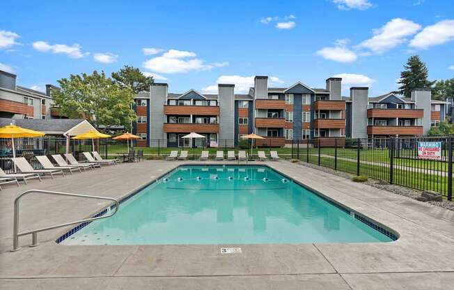 A large outdoor swimming pool with a concrete floor and a metal fence surrounding it. at Northpoint Apartments, Tacoma