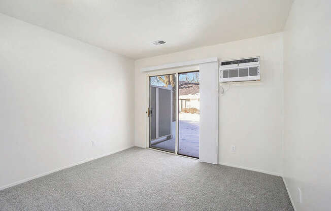 A room with a grey carpet and a white wall with a door leading outside.