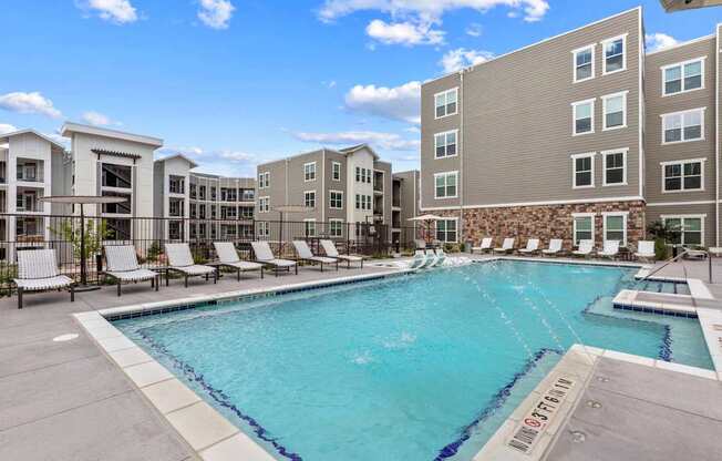 A swimming pool surrounded by lounge chairs and buildings.