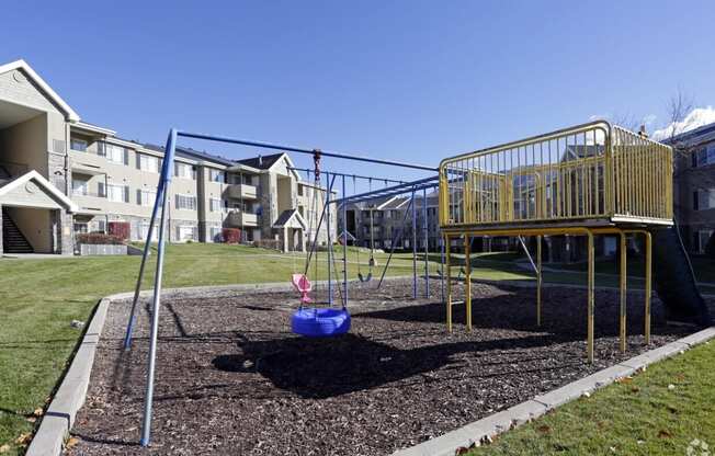 a playground with a swing set and playset in front of an apartment building