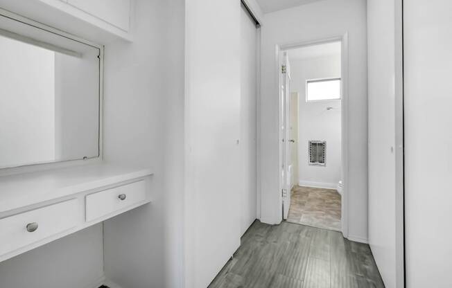 a white room with a mirror and a hallway to a bathroom