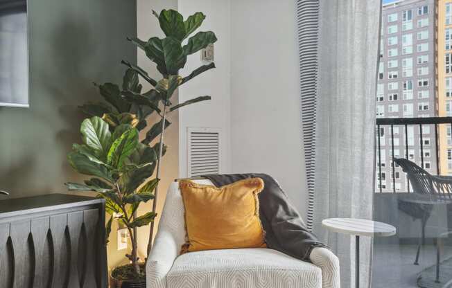 a chair with a yellow pillow in a room with a window and a plant