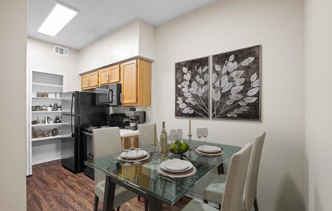 a dining area with a glass table and chairs and a kitchen in the background