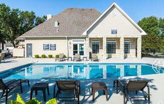 A poolside lounge area with chairs and tables is in front of a house.