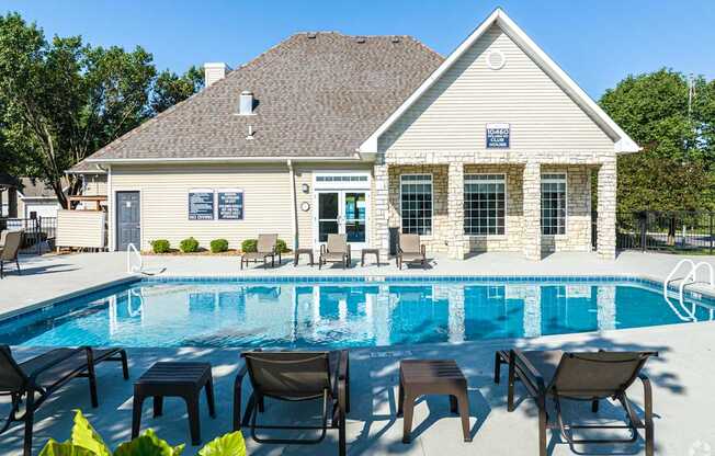 A poolside lounge area with chairs and tables is in front of a house.
