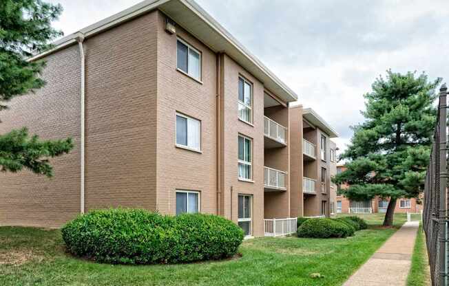 A brown brick apartment building with green bushes in front.